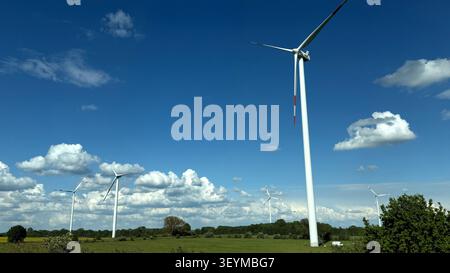 Turbine eoliche alte in un campo verde sotto un cielo blu luminoso con soffici nuvole bianche Foto Stock