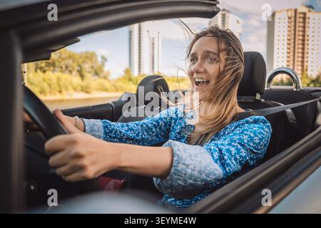 Giovane donna spaventata che urla mentre guida una decappottabile. Fobia della guida, panico dei guidatori principianti e apprendimento nervoso. Stress della lezione di guida. Foto Stock
