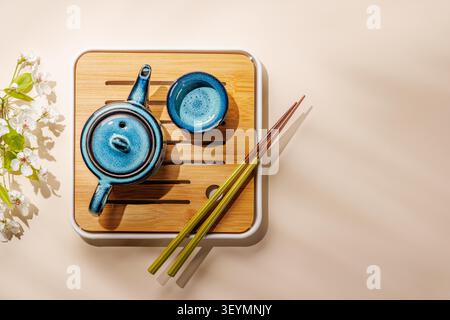 Teiera in ceramica blu con ramoscello primaverile in fiore su vassoio in legno in una composizione minimale in stile asiatico Foto Stock