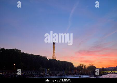 Vista al tramonto della Torre Eiffel a Parigi, vista da una crociera sul fiume Senna, con cielo colorato e sagome di alberi e persone. Parigi, franco Foto Stock