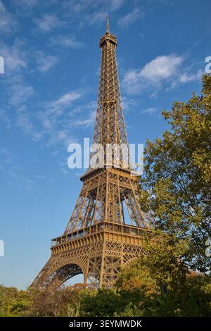 Classica vista diurna della Torre Eiffel che si innalza sopra gli alberi autunnali sotto un cielo blu luminoso a Parigi. Foto Stock