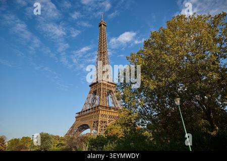 Classica vista diurna della Torre Eiffel che si innalza sopra gli alberi autunnali sotto un cielo blu luminoso a Parigi. Foto Stock