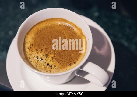 vista dall'alto della tazza da caffè calda nera del mattino con crema marrone sul tavolo scuro Foto Stock