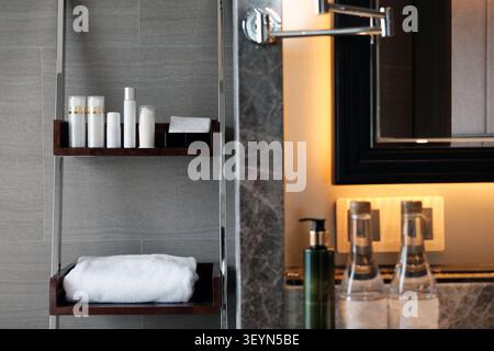 un ripiano con crema per la doccia, balsamo, bottiglie per trattamenti, bottiglia per lozione e asciugamani in un angolo del bagno con doccia vicino a uno specchio Foto Stock