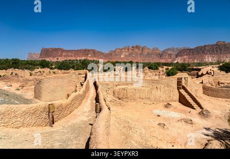 Vista panoramica delle storiche rovine di mattoni di fango della città vecchia di Alula con aspre montagne di arenaria sullo sfondo dell'Arabia Saudita. Foto Stock