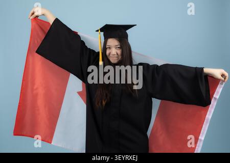 Giovane donna in abito da laurea a braccia aperte che celebra il successo Foto Stock
