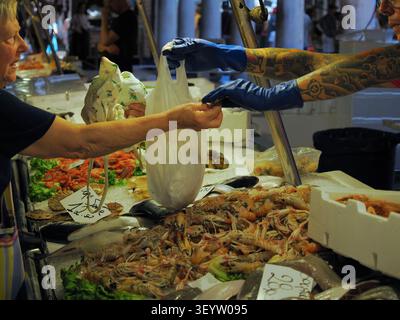 Venezia, Italia - 30 maggio 2026: Il cliente riceve l'acquisto in busta di plastica dal pescivendone al mercato del pesce Foto Stock
