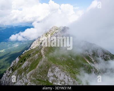 Vista aerea dei monti Piatra Craiului con creste rocciose di pietra calcarea, verdi prati alpini e nuvole alla deriva a Zarnesti, Brasov, Romania. Foto Stock