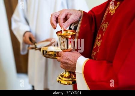 Sacerdote cattolico che prepara l'Eucaristia durante la cerimonia della Santa Comunione, tenendo calice d'oro in chiesa durante il servizio religioso cristiano Foto Stock