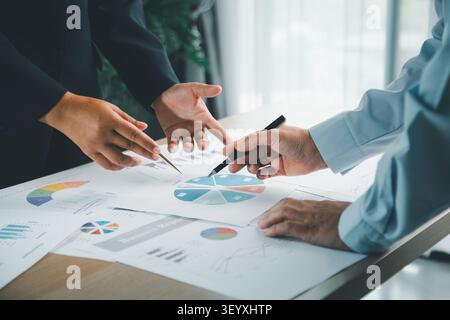 Il team aziendale indica i grafici finanziari e il grafico a torta sulla scrivania dell'ufficio, analizza i dati per il report contabile, la strategia di budget, la pianificazione degli investimenti e Foto Stock