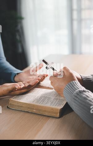 Mani che pregano e tengono una croce di legno su una Bibbia aperta su una tavola di legno, culto cristiano, fede, guida spirituale, speranza, e benedizione Foto Stock