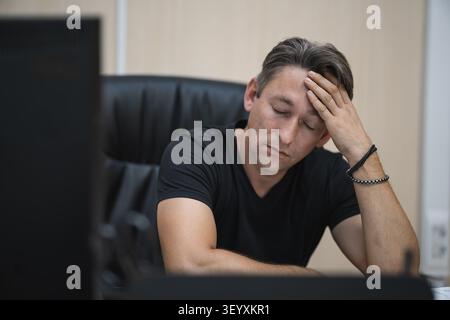 Fatica e burnout sul posto di lavoro. Uomo stanco e stressato alla scrivania che si tiene la testa. Foto Stock
