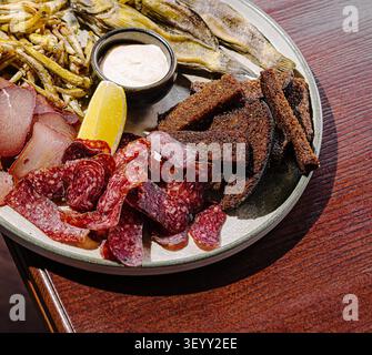 Un piatto colorato con vari spuntini tradizionali, tra cui pesce, carne e pane croccante, guarnito con una spiccata di limone. Perfetto per una riunione informale. Foto Stock
