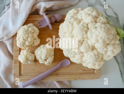 cavolfiore esposto su un tagliere di legno con un panno e utensili in una cucina pulita con una prospettiva dall'alto verso il basso, colori bianco e marrone Foto Stock