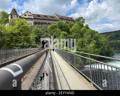 Sentiero pedonale e binario ferroviario sul ponte che porta a un tunnel sotto Schloss Laufen alle cascate del Reno Foto Stock