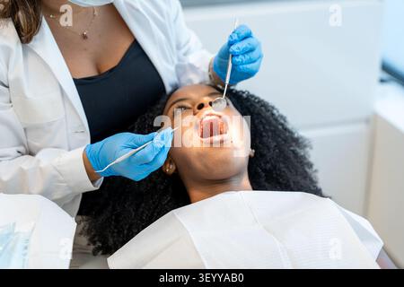 Dentista che indossa guanti blu che esaminano i denti di una giovane donna per l'igiene orale e la salute Foto Stock