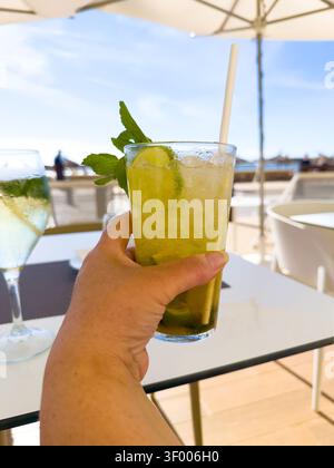 Tenere a mano un cocktail di mojito freddo con lime e menta su un tavolo all'aperto Foto Stock