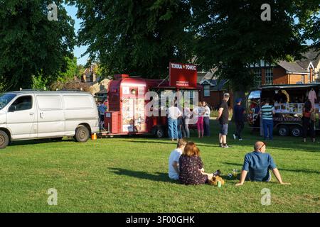 Persone che si godono una giornata di sole al parco con camioncini alimentari a Saffron Walden Foto Stock