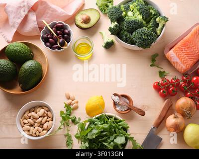 Gli ingredienti freschi sono disposti su un tavolo di legno in una cucina. Tra i prodotti sono inclusi broccoli, salmone, avocado, olive ed erbe pronte per cucinare un sano Foto Stock