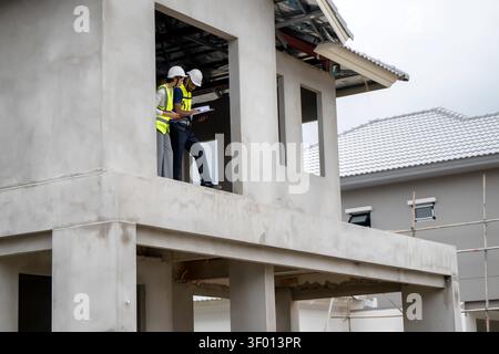 I responsabili edili controllano gli appunti sul balcone del secondo piano di una casa residenziale incompiuta durante il giorno, il concetto di gestione dei progetti e il tè Foto Stock