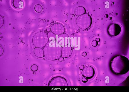 Vivace macro viola di bolle d'olio che galleggiano nel liquido, formando motivi circolari organici e luci lucide. Background astratto ideale per la scienza, Foto Stock