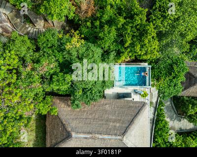 Vista aerea di un viaggiatore che si rilassa in una piscina a sfioro privata accanto a una villa tropicale, circondato da lussureggiante vegetazione della giungla a Koh Tao, Thailandia, durante Foto Stock