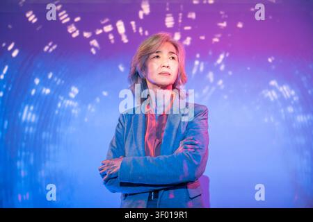 Donna asiatica con un blazer sicura di sé con le braccia incrociate sotto la luce blu neon e viola, circondata da modelli digitali astratti, futuristici Foto Stock
