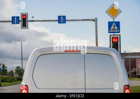 Veicolo per consegne bianche parcheggiato in un incrocio a semaforo rosso con segnaletica di guida corsia sopraelevata e un cartello di avvertenza per attraversamento pedoni nella c Foto Stock