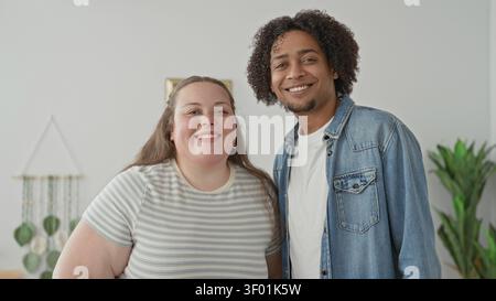 Uomo e donna più taglia staranno vicini, con volti sorridenti, uomo con giacca in denim e donna con camicia a righe all'interno di un edificio luminoso; gioia di stare insieme. Foto Stock