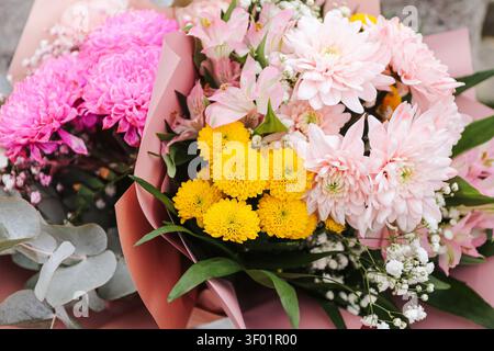 Mazzi colorati di fiori rosa, bianchi e gialli avvolti in carta decorativa. Sfondo floreale per celebrazione, auguri di compleanno, regalo e speciale. Foto Stock
