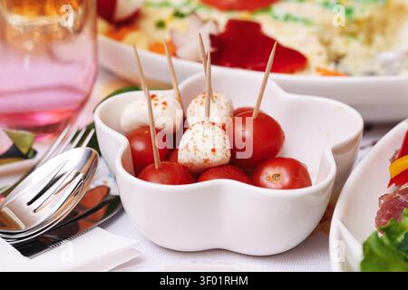 Piccoli antipasti di formaggio su spiedini di legno serviti in una ciotola bianca sul tavolo della festa. Sfondo di finger food per snack da buffet per feste di catering. Foto Stock