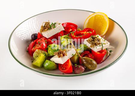 Vivace insalata greca con feta, pomodori rossi, cetrioli verdi, olive, capperi, fetta di limone. Colori brillanti, composizione pulita, luci da studio Foto Stock