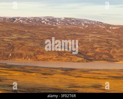 Vista aerea dell'aspro paesaggio vulcanico con colline ondulate, macchie di neve e un lago calmo sotto la luce soffusa dell'ora d'oro a Reykjanes Foto Stock