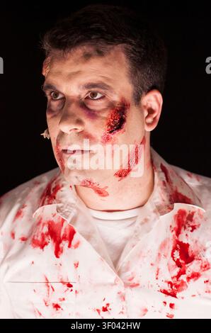 Spaventoso zombie ricoperto di pose di sangue su uno sfondo nero, che mostra un trucco creativo e un spaventoso look di Halloween, con uno stile da studio isolato e dettagli sui costumi scuri. Foto Stock