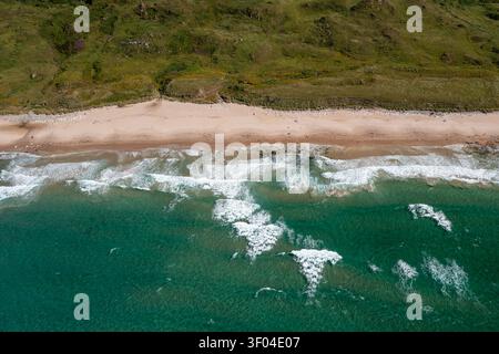 Splendida vista di una spiaggia sabbiosa e di una costa rocciosa con onde turchesi che si infrangono sulla riva sotto verdi scogliere erbose, che trasmettono la calma costiera, Antrim Foto Stock