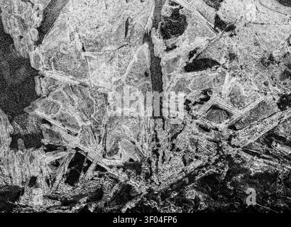 Sfondo: risorsa grafica di arte naturale. Ghiaccio su una pozzanghera ghiacciata in bianco e nero a bassa luminosità. Foto Stock
