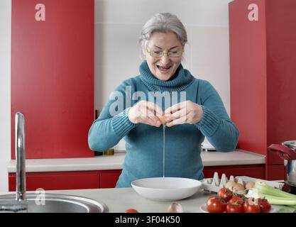 Donna anziana felice che spacca un uovo in una ciotola Foto Stock