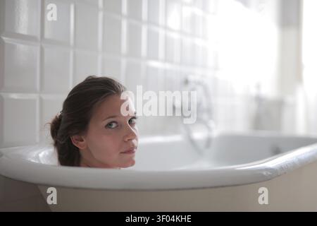 Donna che si guarda alle spalle nella vasca da bagno Foto Stock