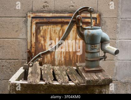 Vecchia pompa dell'acqua manuale in ghisa resistente agli agenti atmosferici montata su un bacino in pietra rustica fuori da un muro, Kyoto, Giappone Foto Stock