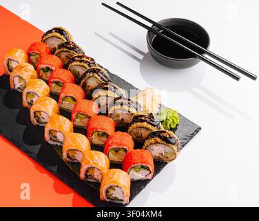 Panini di sushi disposti su un piatto nero con salsa di soia e bacchette Foto Stock