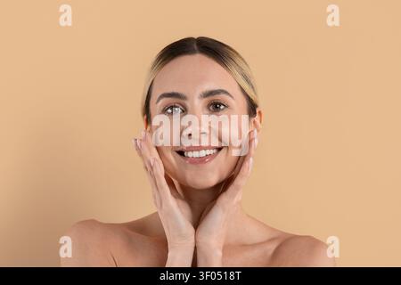 Giovane donna bella che sorride e si tocca le guance con entrambe le mani Foto Stock