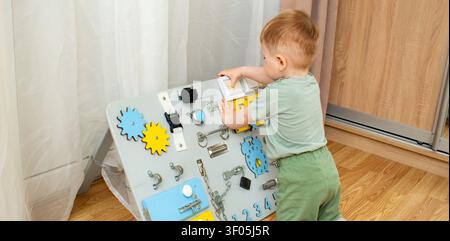 Bambino di due anni che gioca con una tavola occupativa a casa. Sviluppo della motricità fine attraverso un'esplorazione sicura. Educazione precoce attraverso il tatto Lea Foto Stock
