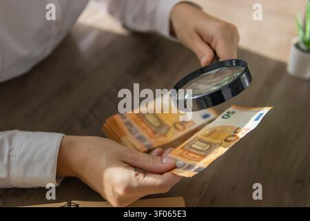 Persona che utilizza una lente d'ingrandimento per esaminare attentamente una banconota da 50 euro alla ricerca di segni di contraffazione, simboleggiando la verifica finanziaria e la prevenzione delle frodi Foto Stock