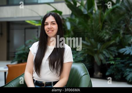 Giovane donna seduta in una lounge moderna dell'ufficio con piante verdi rigogliose. Benessere dei dipendenti e design biofilico del posto di lavoro. Foto Stock