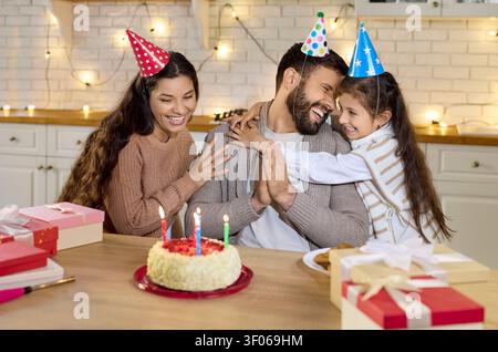 Famiglia felice che festeggia la festa di compleanno in casa, genitori e figlia ridono e abbracciano Foto Stock