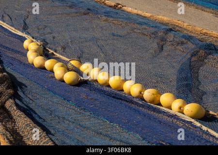 Primo piano di una rete da pesca blu con galleggianti gialli e corda disposti ad asciugare su una spiaggia sabbiosa, mostrando consistenza, equipaggiamento marittimo e pesca costiera indo Foto Stock