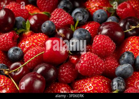 Vivace primo piano di mix di bacche fresche con fragole, lamponi, mirtilli e ciliegie dolci. Colorato sfondo di frutta estiva con succose Foto Stock