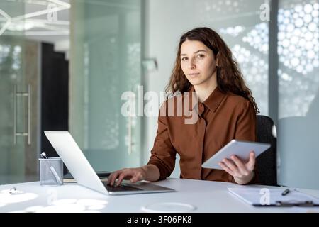 Giovane donna d'affari multitasking con laptop e tablet digitale in un ufficio moderno Foto Stock