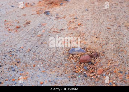 Piccole pietre e frammenti di argilla arancione sono sparsi sulla superficie asciutta e sabbiosa della strada. Strada sterrata di campagna con una trama sabbiosa e tracce di pneumatici Foto Stock