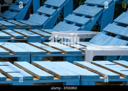 File di lettini in legno blu con tavolini bianchi disposti in un'area di relax all'aperto, creando un motivo geometrico per il tempo libero e l'estate Foto Stock